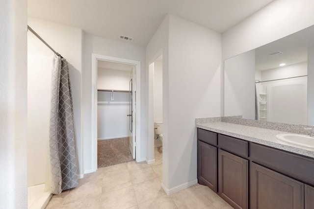 full bathroom with a walk in closet, visible vents, toilet, vanity, and baseboards