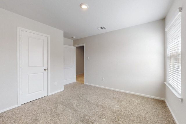 empty room featuring baseboards, visible vents, and light colored carpet