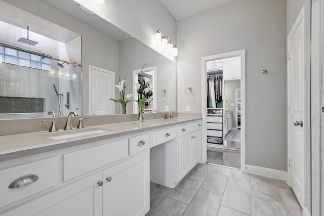 bathroom with double vanity, a walk in closet, a sink, and tiled shower