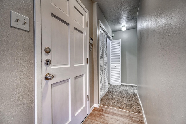 hall with a textured ceiling, baseboards, and a textured wall
