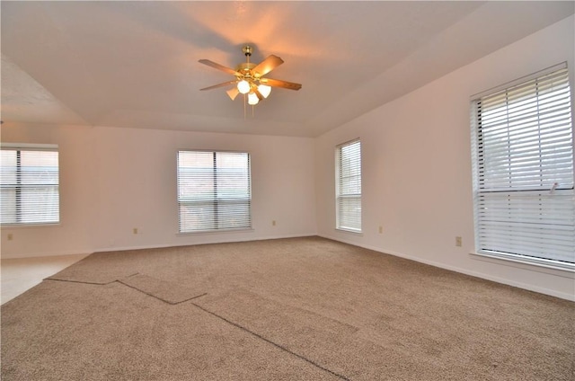 carpeted empty room with a ceiling fan, a tray ceiling, and baseboards