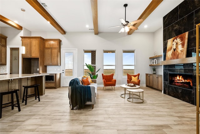 living area featuring visible vents, ceiling fan, beamed ceiling, light wood-style floors, and a high end fireplace