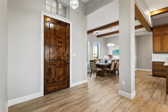 entrance foyer with baseboards, light wood-style floors, beamed ceiling, and an inviting chandelier