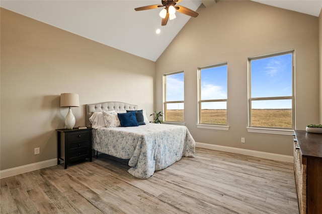 bedroom featuring light wood finished floors, ceiling fan, baseboards, and high vaulted ceiling