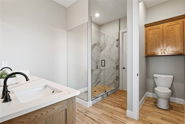 bathroom with toilet, wood finished floors, a sink, baseboards, and a marble finish shower