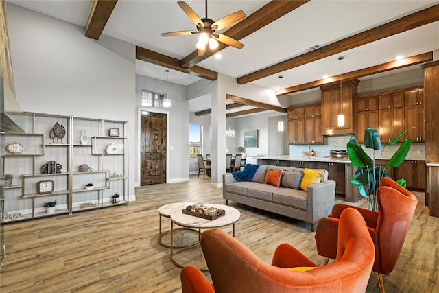 living area featuring light wood finished floors, ceiling fan, baseboards, and beamed ceiling