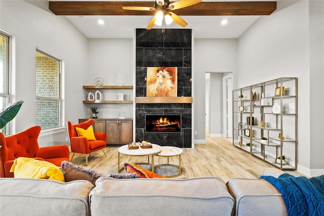 living room with a tile fireplace, wood finished floors, a ceiling fan, baseboards, and beamed ceiling