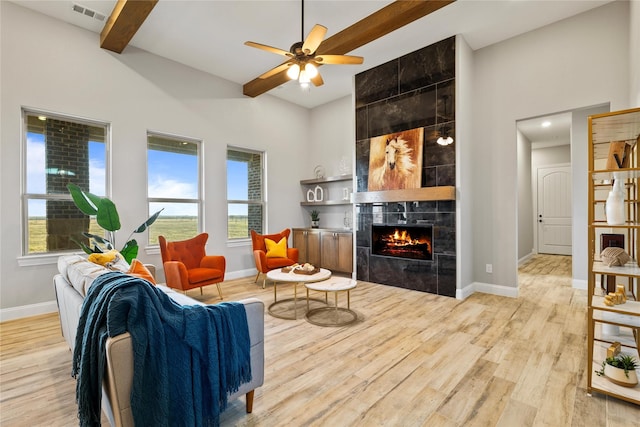 living area featuring light wood-style flooring, a tiled fireplace, visible vents, and baseboards