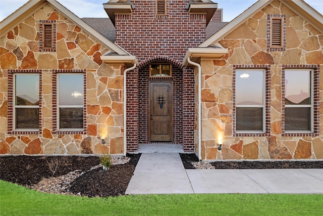 property entrance with a shingled roof, stone siding, and brick siding