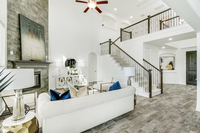 living room with ceiling fan, arched walkways, a tile fireplace, visible vents, and stairway