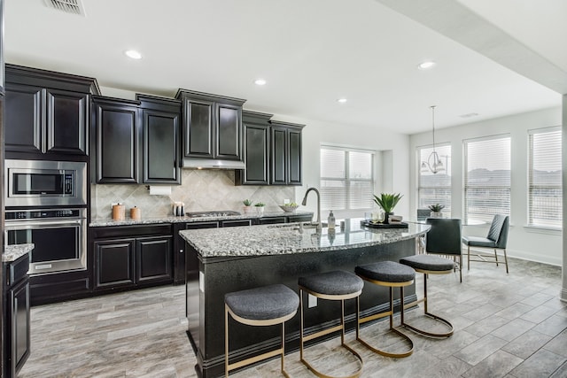 kitchen featuring appliances with stainless steel finishes, a sink, dark cabinets, and tasteful backsplash