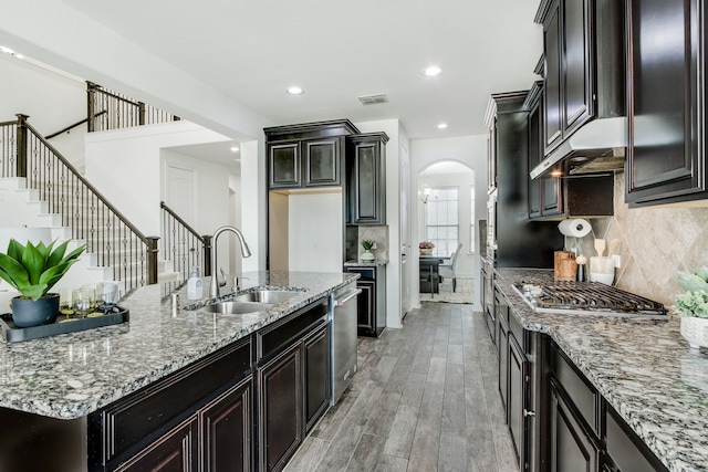 kitchen featuring arched walkways, under cabinet range hood, a sink, light wood-style floors, and backsplash