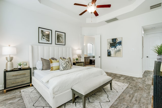 bedroom with light wood-type flooring, baseboards, visible vents, and a raised ceiling