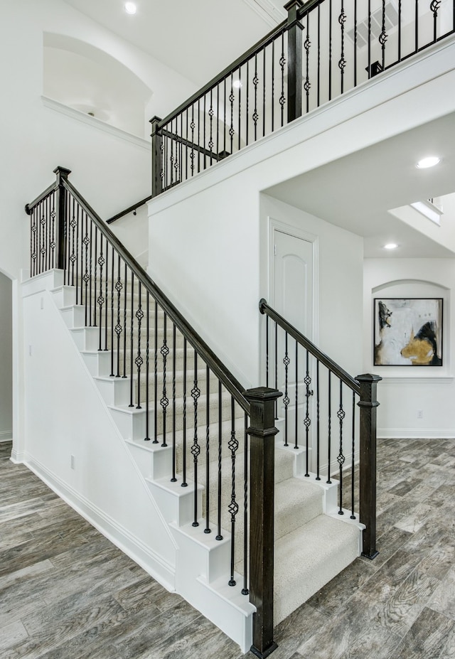 stairs featuring recessed lighting, a towering ceiling, baseboards, and wood finished floors