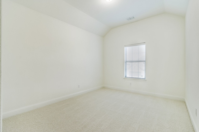 spare room with lofted ceiling, baseboards, visible vents, and light colored carpet