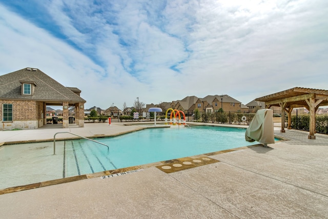 community pool with a patio area, fence, a water play area, and a pergola