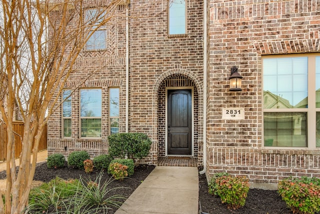 doorway to property with brick siding and fence