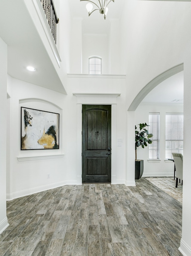 entryway featuring a towering ceiling, baseboards, arched walkways, and wood finished floors