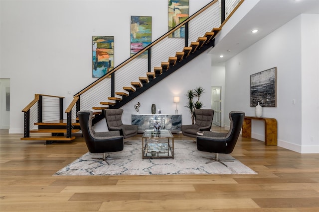 living area with stairway, baseboards, a towering ceiling, and wood finished floors