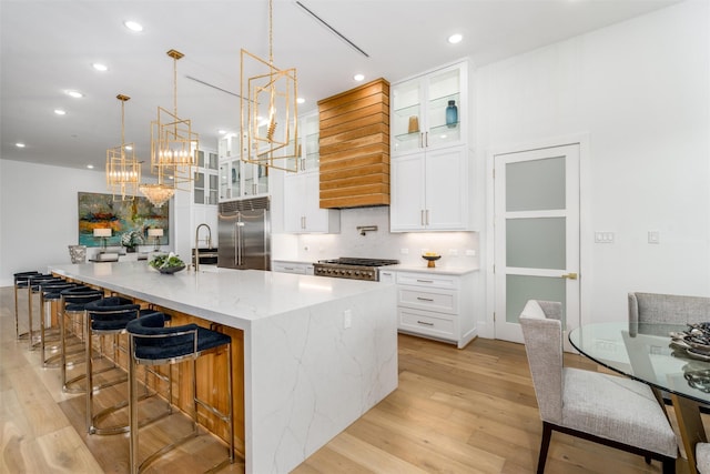 kitchen with a chandelier, light wood-type flooring, decorative backsplash, a large island, and built in fridge