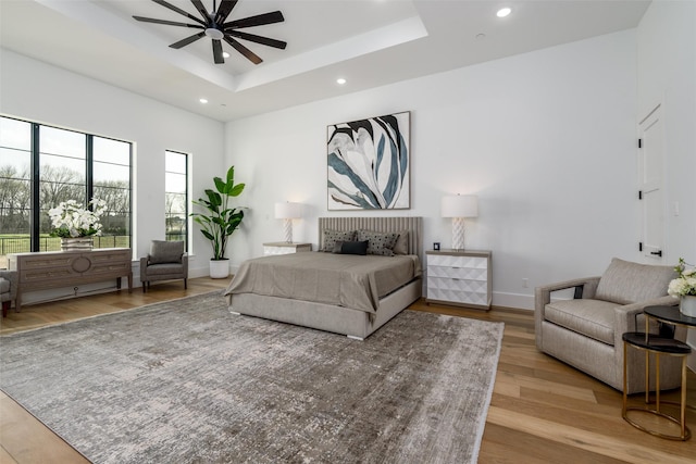 bedroom with a raised ceiling, recessed lighting, light wood-style floors, and baseboards