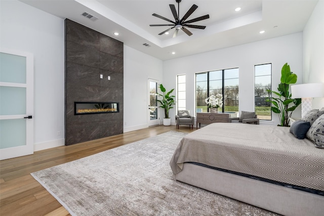 bedroom with visible vents, wood finished floors, baseboards, a fireplace, and a raised ceiling