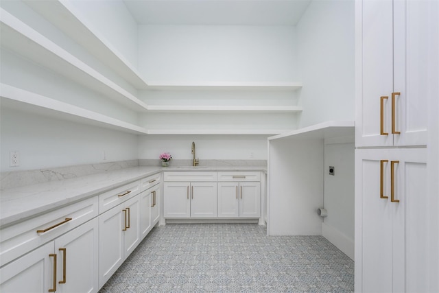 interior space with light floors, light stone countertops, open shelves, a sink, and white cabinets