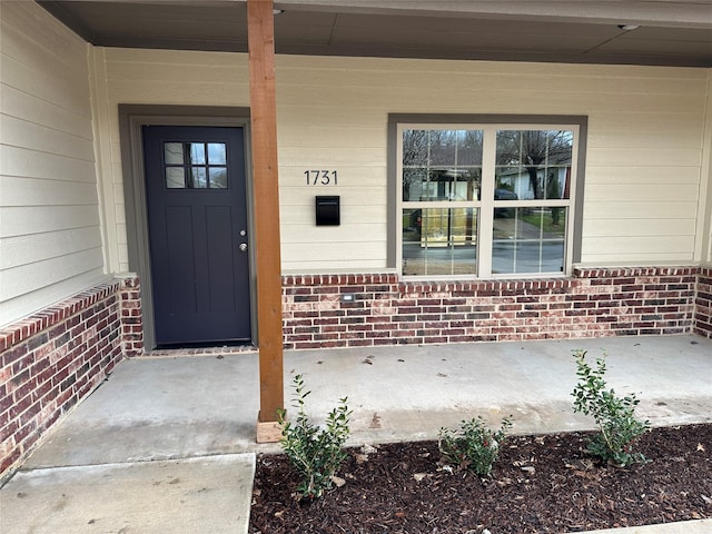 entrance to property featuring covered porch and brick siding