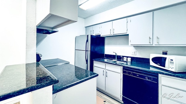 kitchen featuring white microwave, freestanding refrigerator, a sink, wall chimney range hood, and dishwasher