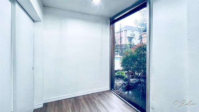 unfurnished room with a textured ceiling, a wall of windows, wood finished floors, and baseboards