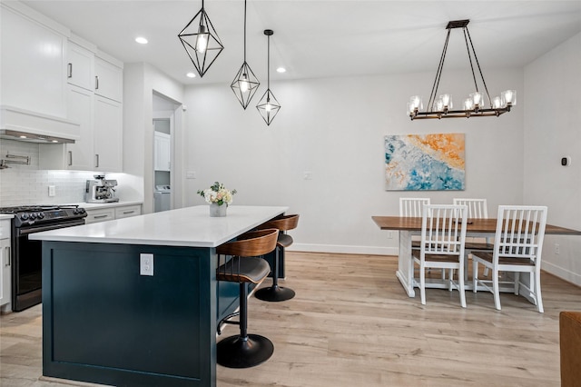 kitchen featuring light wood-style flooring, a kitchen breakfast bar, backsplash, range with gas cooktop, and white cabinets