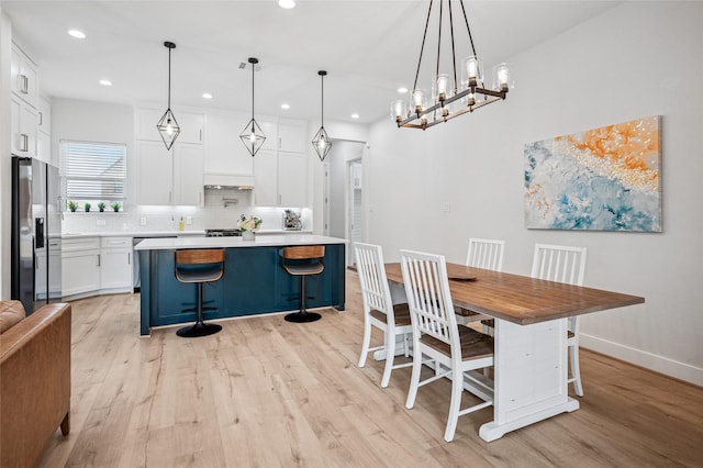 kitchen with tasteful backsplash, light wood finished floors, a kitchen bar, stainless steel fridge, and white cabinetry