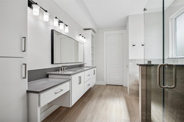 full bathroom with a shower stall, wood finished floors, double vanity, and a sink