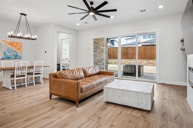 living room featuring baseboards, light wood finished floors, recessed lighting, a glass covered fireplace, and ceiling fan with notable chandelier