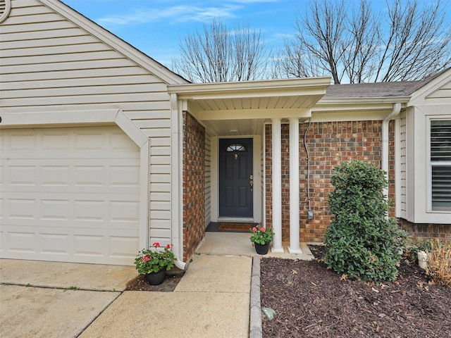 entrance to property featuring an attached garage, driveway, roof with shingles, and brick siding