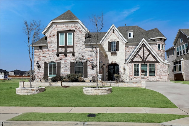 view of front facade with a shingled roof, a front lawn, and brick siding