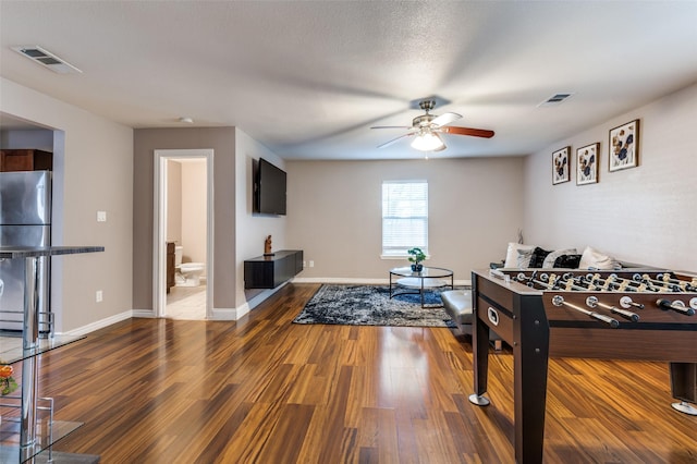 recreation room featuring a ceiling fan, visible vents, baseboards, and wood finished floors