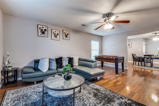 living room with ceiling fan, wood finished floors, visible vents, and baseboards