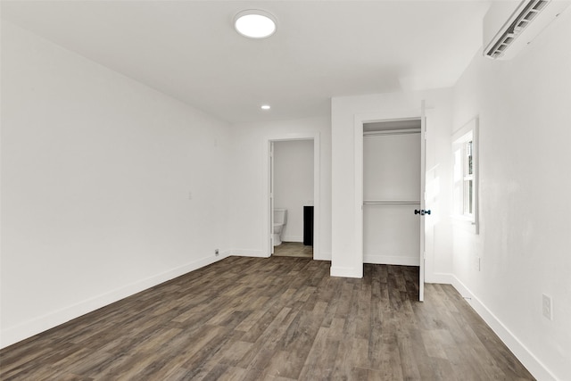 unfurnished bedroom featuring a closet, dark wood-style flooring, a wall mounted air conditioner, and baseboards