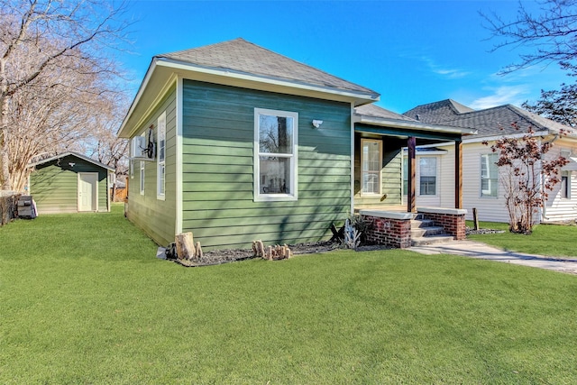 view of front of house with an outbuilding, roof with shingles, a storage unit, and a front yard