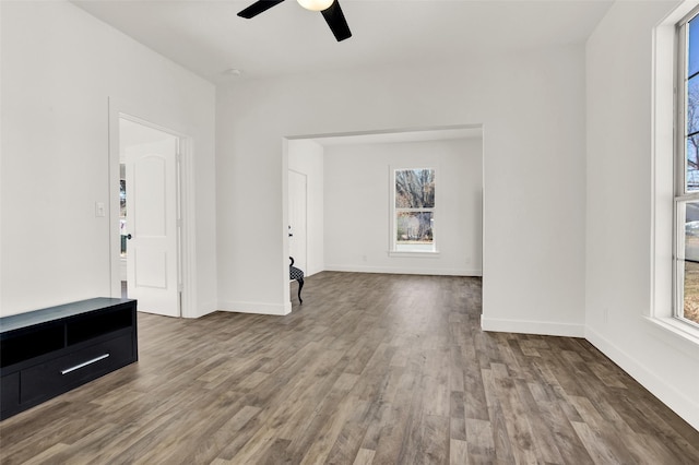 unfurnished living room with ceiling fan, baseboards, and wood finished floors