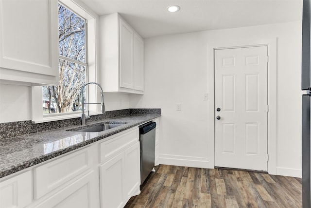 kitchen with dark wood-style flooring, a sink, white cabinetry, stainless steel dishwasher, and dark stone countertops