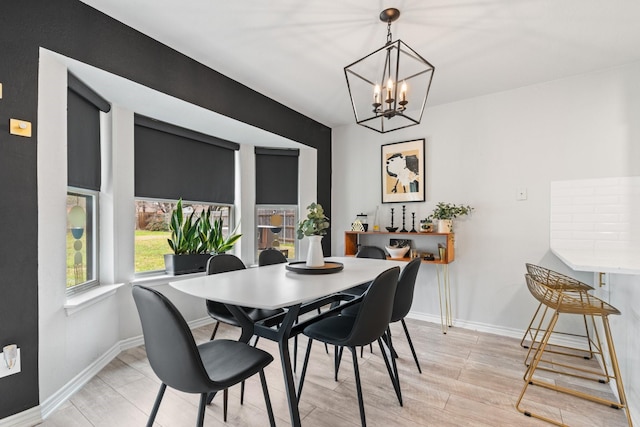 dining area with light wood-style flooring, baseboards, and a notable chandelier