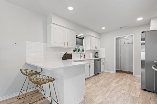 kitchen with appliances with stainless steel finishes, a peninsula, light countertops, white cabinetry, and a sink