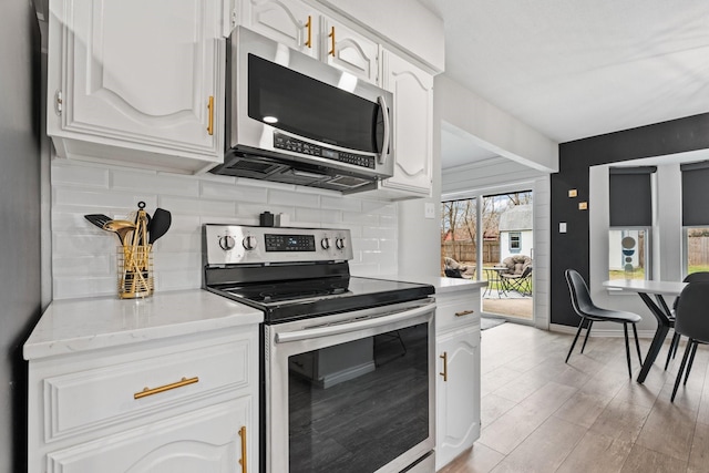 kitchen featuring appliances with stainless steel finishes, white cabinets, light wood finished floors, and tasteful backsplash