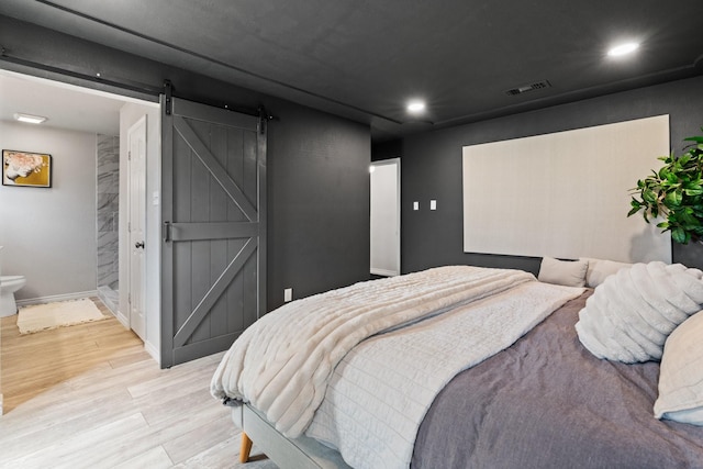 bedroom with recessed lighting, visible vents, a barn door, light wood-type flooring, and baseboards