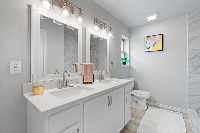 bathroom featuring double vanity, toilet, a tile shower, and a sink