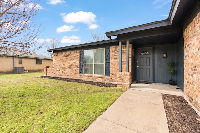 doorway to property with a yard, brick siding, and central AC