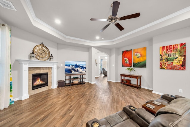 living room featuring arched walkways, light wood-style flooring, visible vents, a tray ceiling, and crown molding