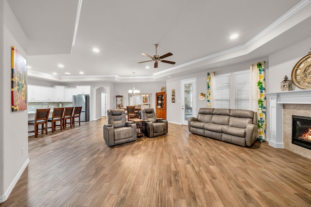 living room featuring a tile fireplace, light wood-style flooring, recessed lighting, ornamental molding, and a raised ceiling